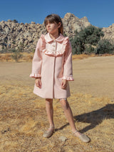 Young girl in a pink coat standing in a desert landscape with rocky formations.